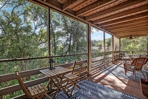 A covered outdoor area with wooden furniture, a patterned rug, and large windows offering a view of trees. - Secluded Condo with Peaceful Wooded Views and Easy Access to the Beach by RedAwning (Fernandina Beach)