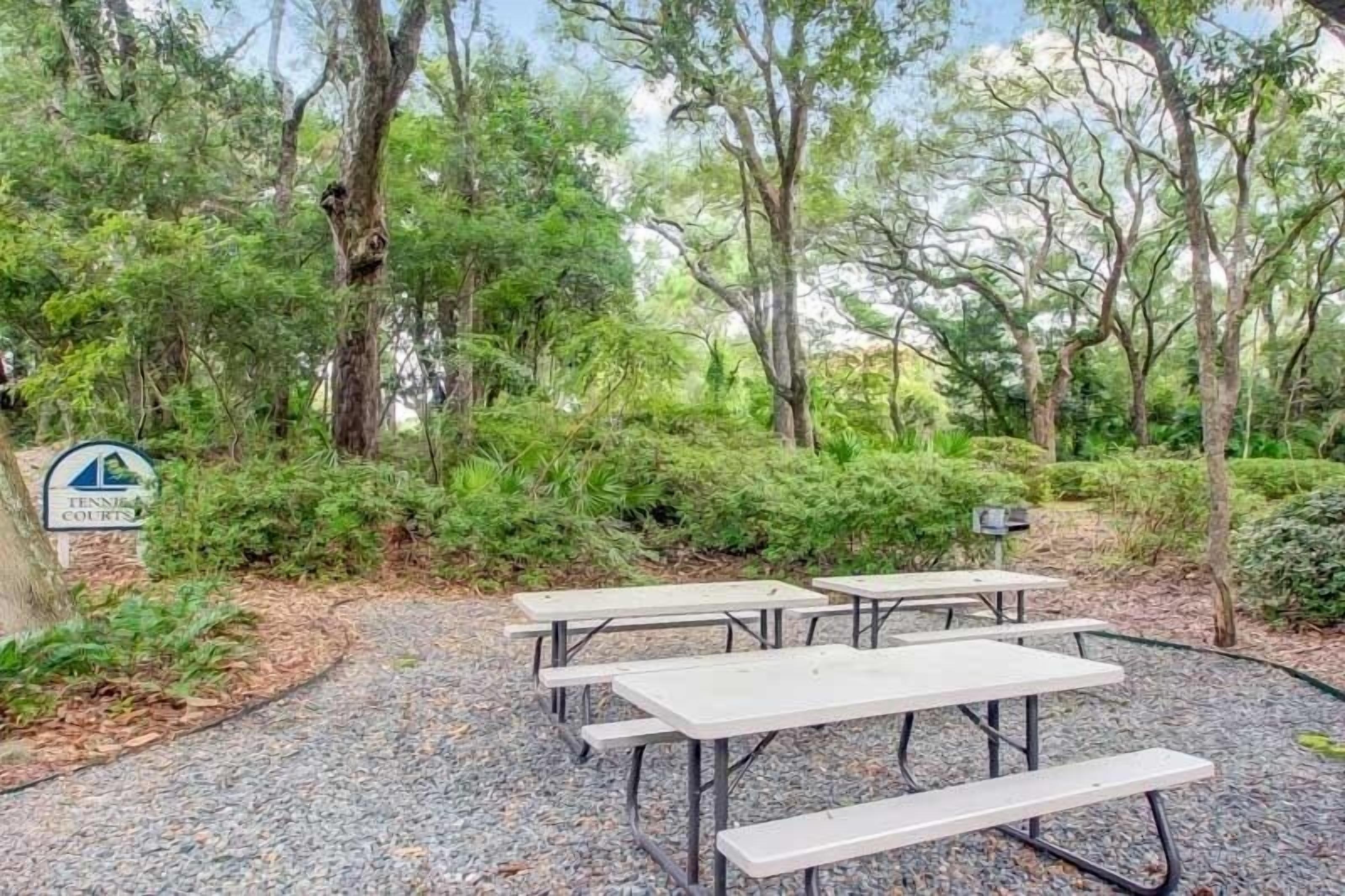 Un espacio al aire libre con mesas de picnic rodeado de abundante vegetación y árboles.