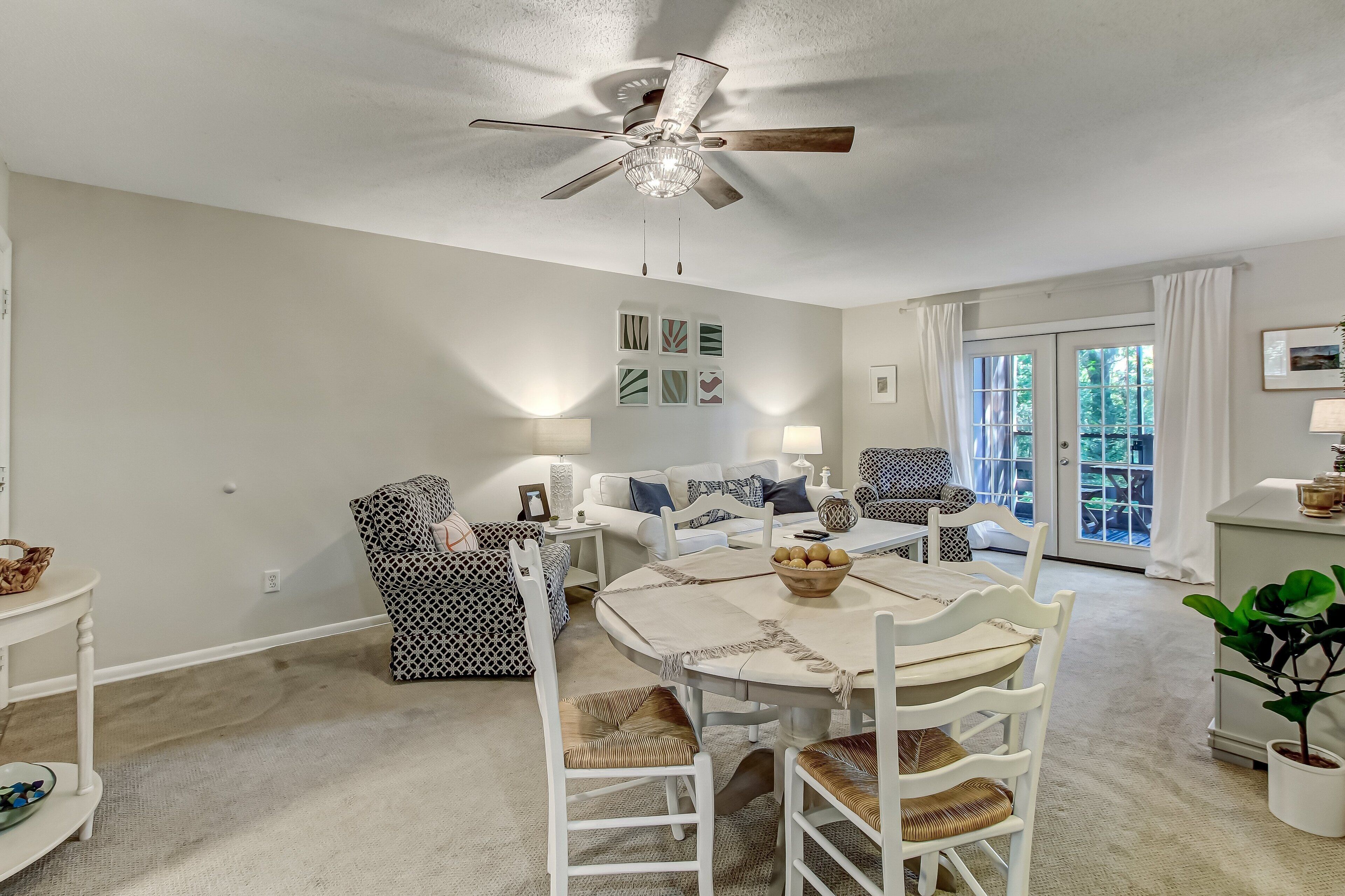 A dining area with a white table and chairs, a ceiling fan, and a view of the outdoors through a glass door.