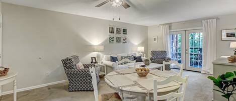 A dining area with a white table and chairs, a ceiling fan, and a view of the outdoors through a glass door.
