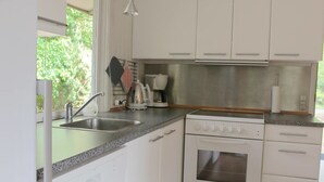 A kitchen with white cabinets, a stainless steel sink, a stove, and a kettle. - Holiday home Aakirkeby (Akirkeby)