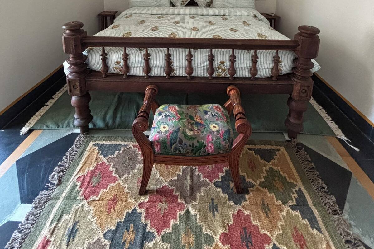A bedroom with a wooden bed, a green upholstered chair, a patterned rug, and a window with a decorative frame.