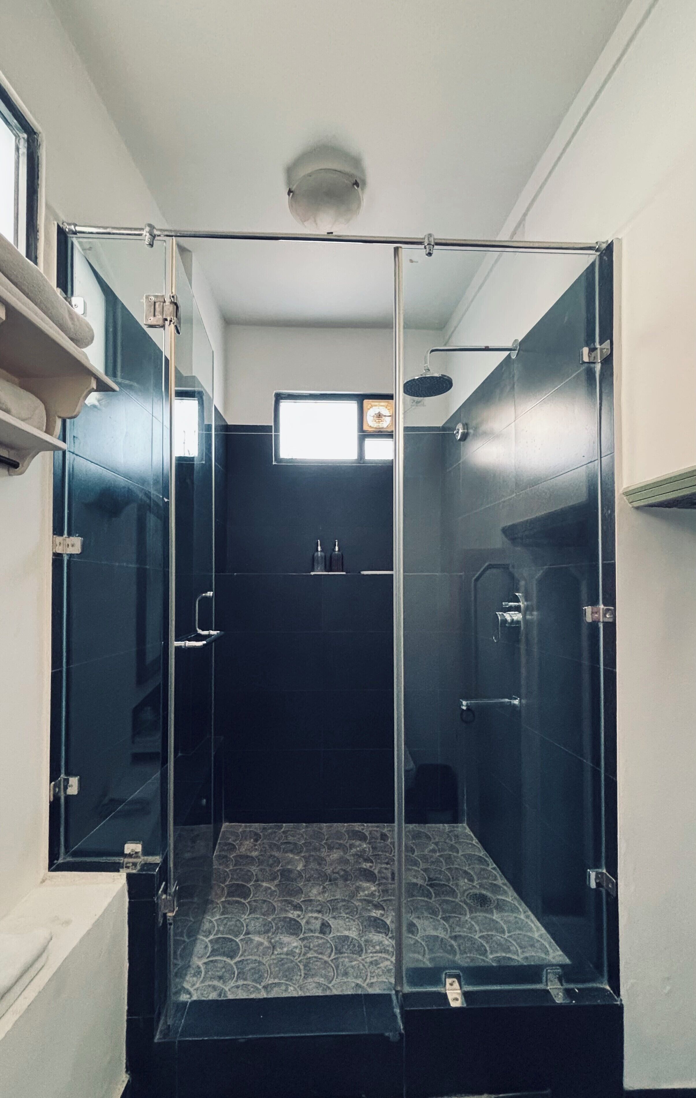 A modern bathroom with a glass-enclosed shower, a small window, and a tiled floor.