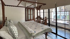 A bedroom with a wooden four-poster bed, a small wooden stool, and a large window providing a view of the outside. - Kintsugi at Rangniwas (Udaipur)