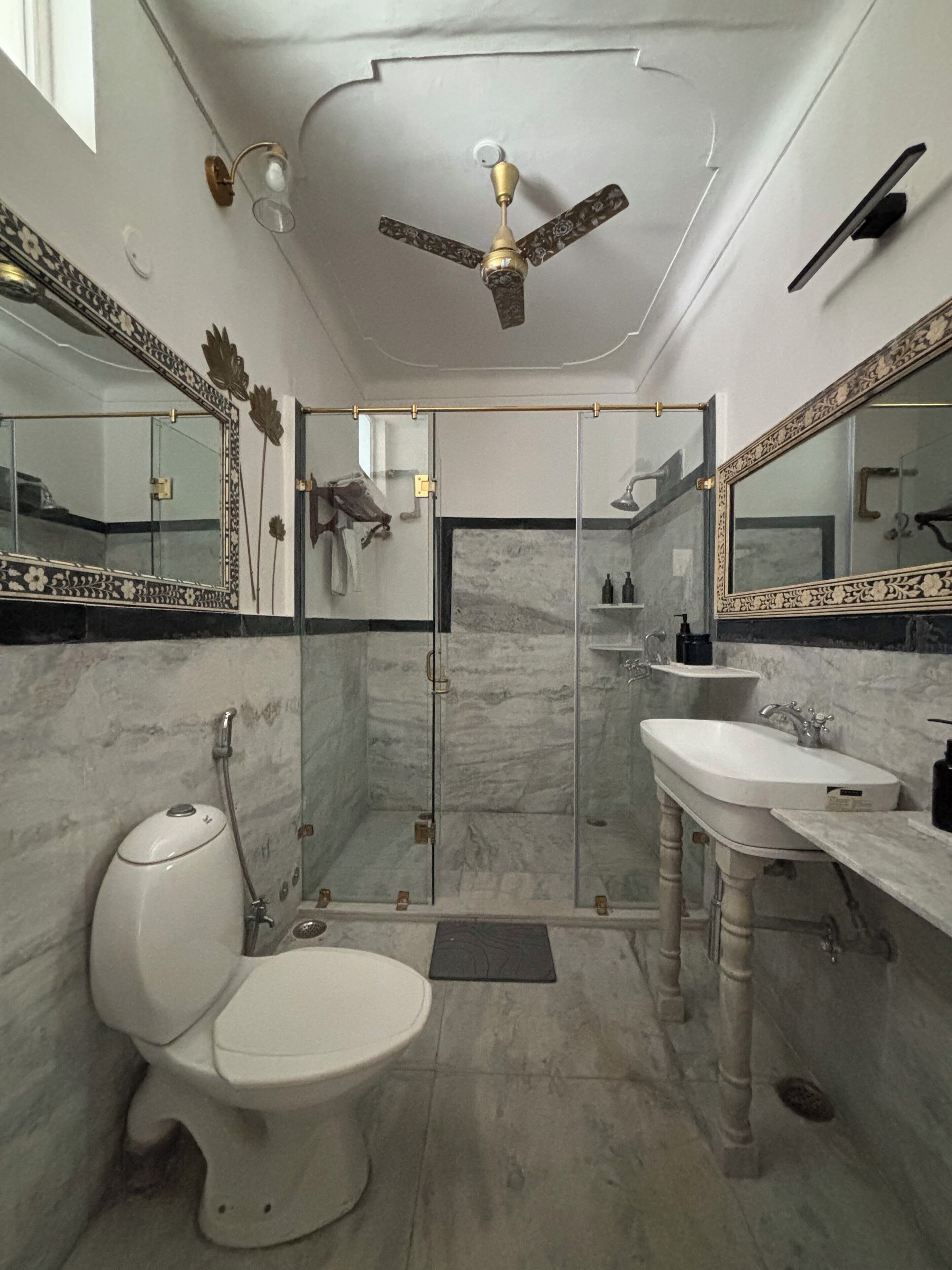 A bathroom with a toilet, two sinks, a shower, and a ceiling fan.