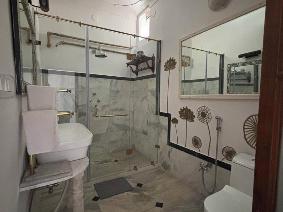 A bathroom with a white sink, a toilet, a shower with a glass door, a ceiling fan, and decorative wall art.