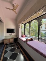 Una habitación con cama, televisión, ventilador de techo y ventana con vistas a la vegetación.