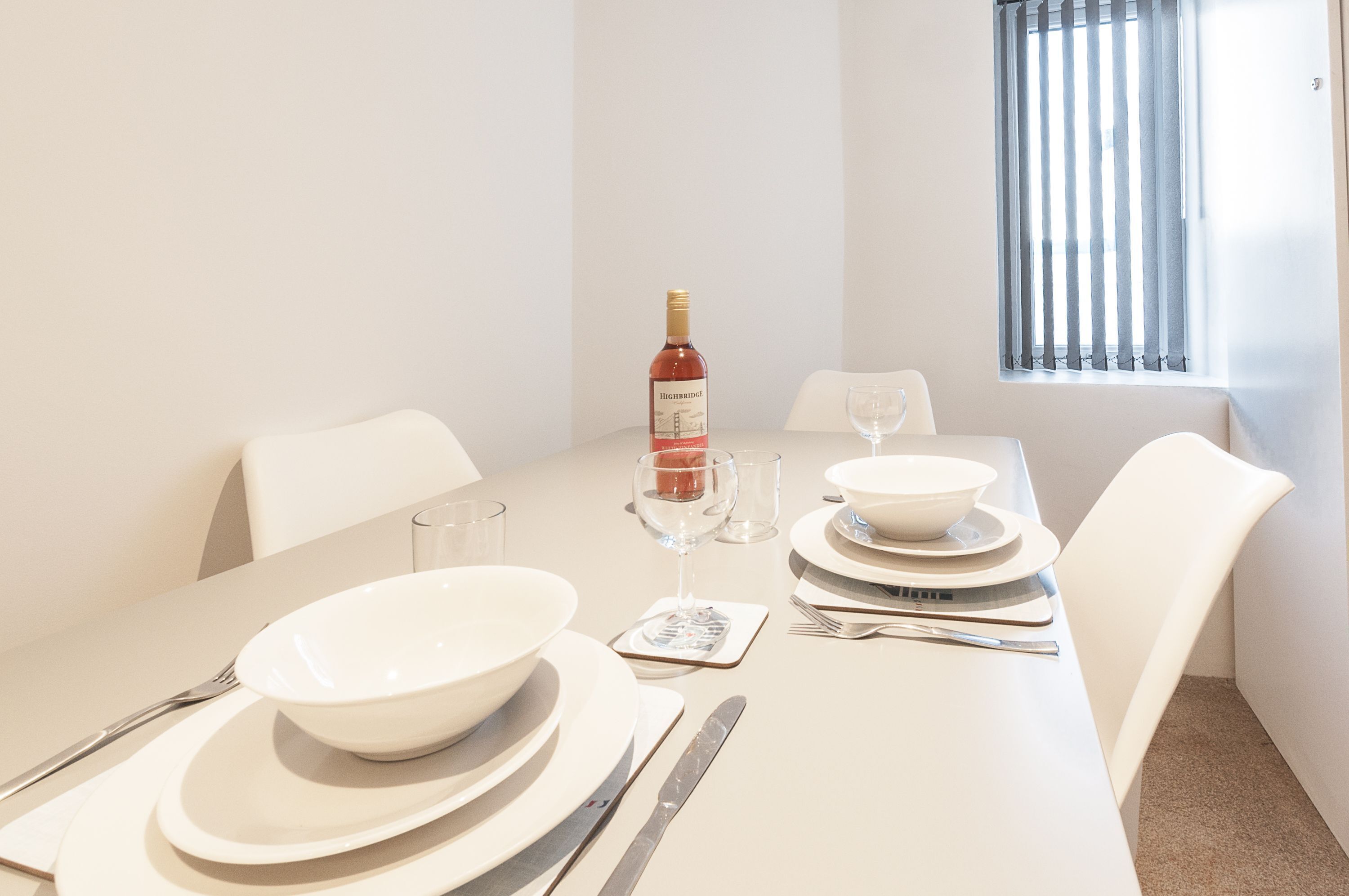 A dining table set with white plates, bowls, cutlery, and a wine bottle.