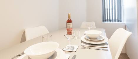 A dining table set with white plates, bowls, cutlery, and a wine bottle.