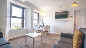 A modern living room with a sofa, a table, and a TV mounted on the wall. - Five Way Apartments (Paignton)