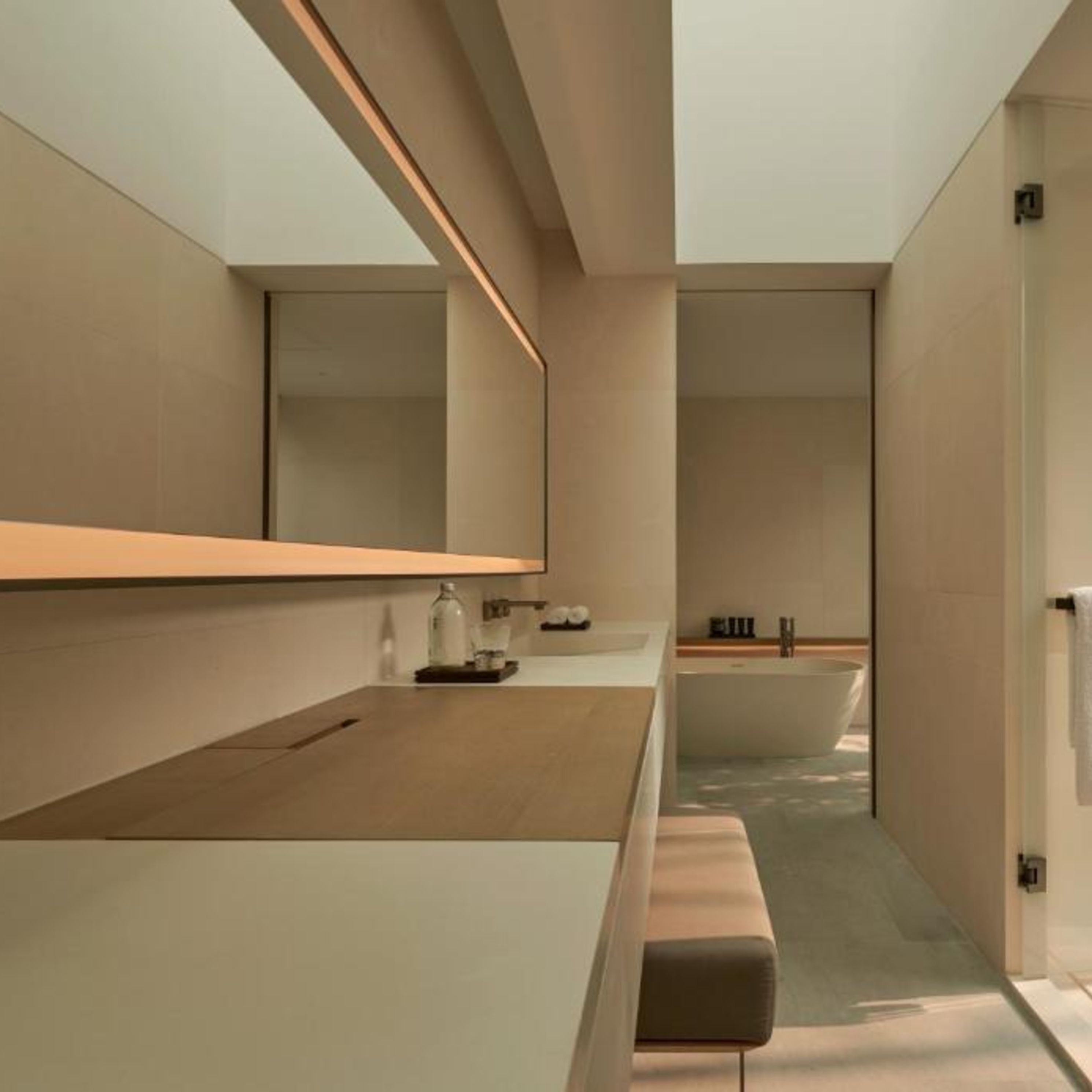 Een moderne badkamer met een grote spiegel, een badkuip en een zitbankje.