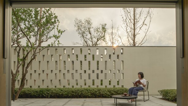 A person sitting on a chair reading a book in an outdoor area with a modern fence and greenery. - Alila Wuzhen, Zhejiang (Jiaxing)