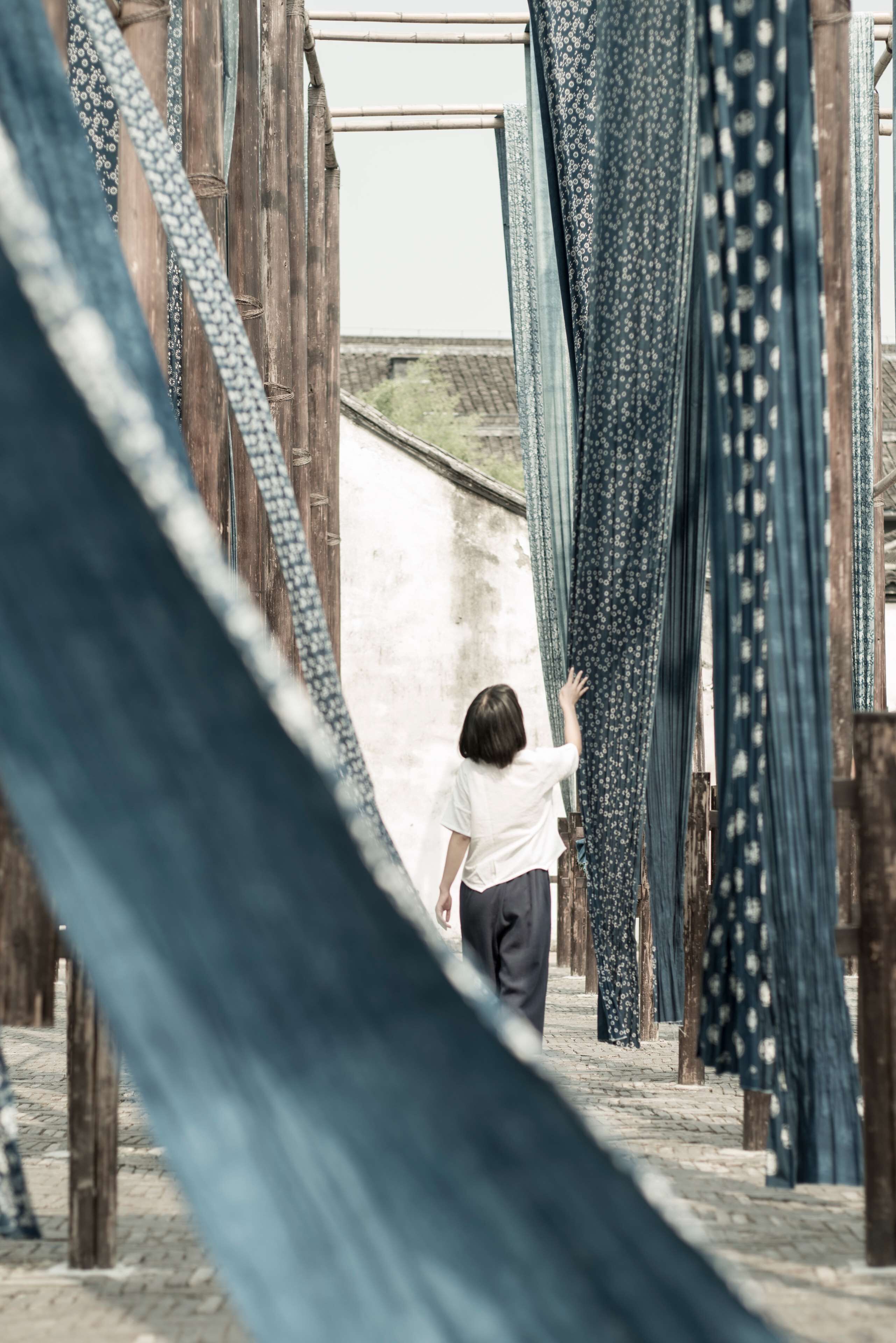 A person walking through a corridor lined with hanging fabrics.