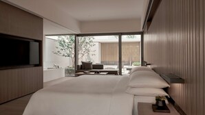 A modern bedroom with a large bed, a TV, and a sliding glass door leading to a balcony with a view of trees and a building. - Alila Wuzhen, Zhejiang (Jiaxing)