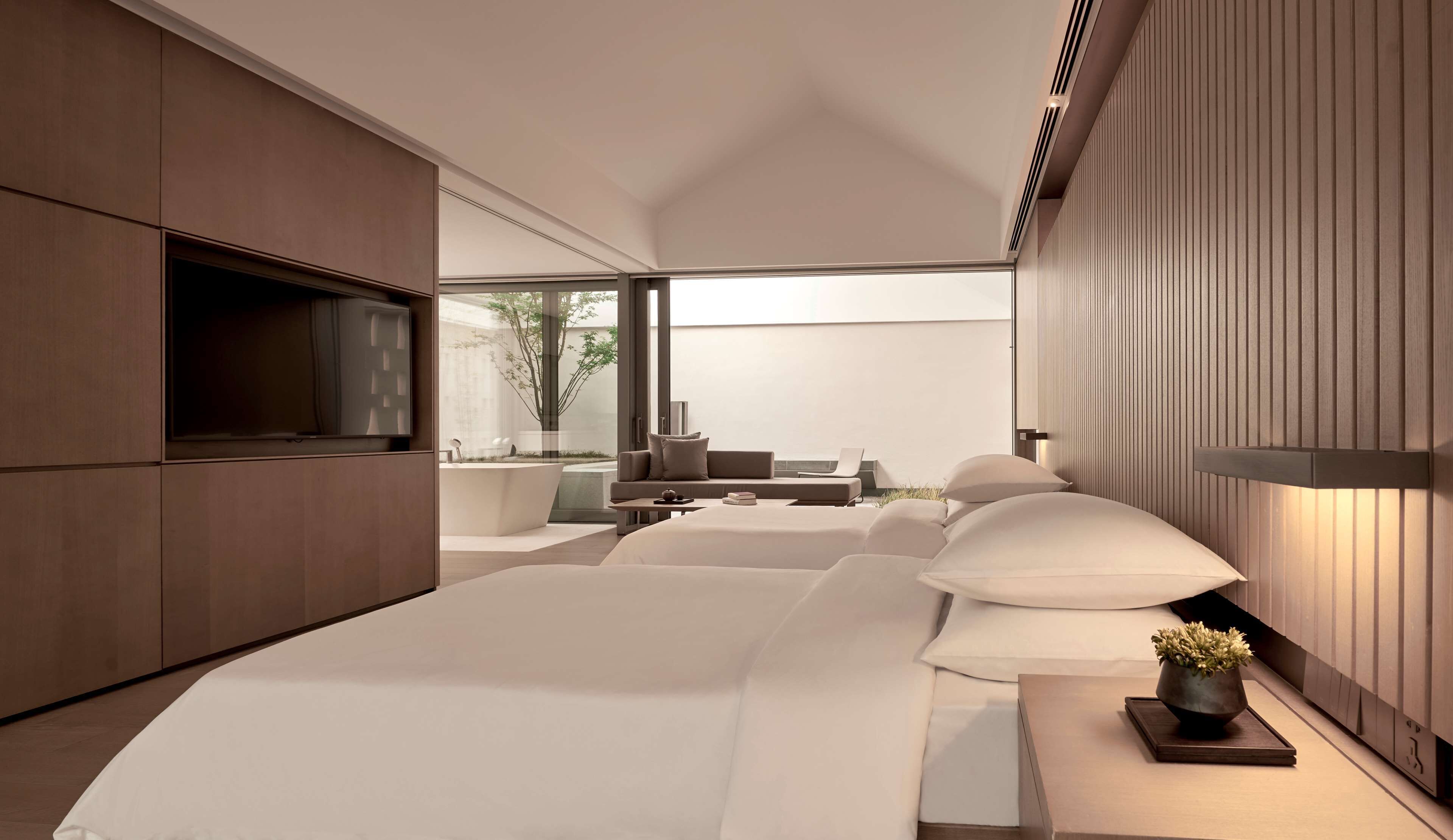 A modern bedroom with a large bed, a TV, and a seating area with a view of the outdoors.