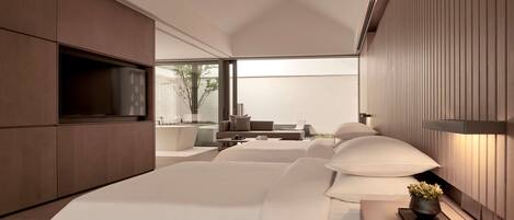 A modern bedroom with a large bed, a TV, and a seating area with a view of the outdoors.