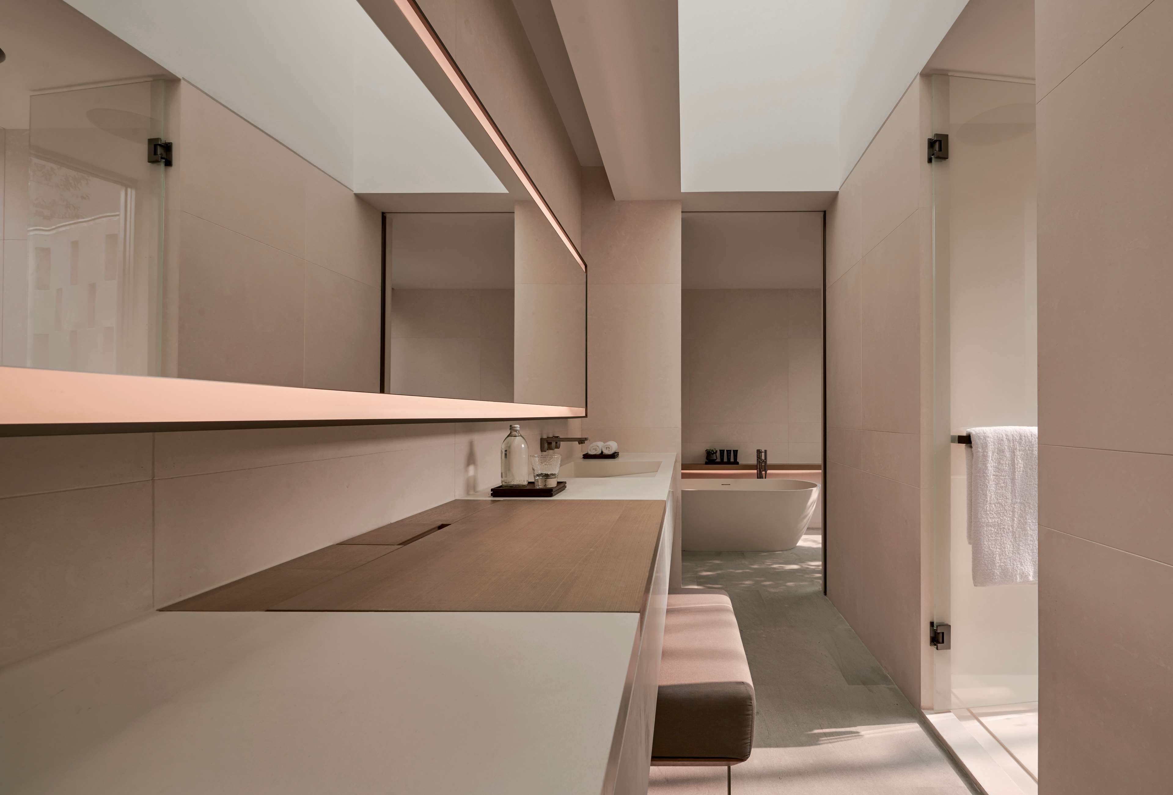 A modern bathroom with a large bathtub, a wooden vanity, and a bench.