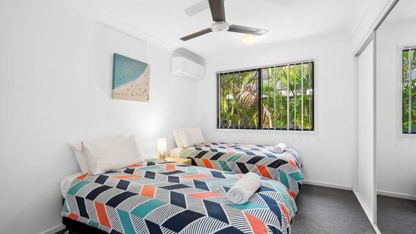 A bedroom with a bed, a ceiling fan, a window with a view of greenery, and a wall-mounted air conditioner. - 252 David Low Way, Peregian Beach (Peregian Beach)