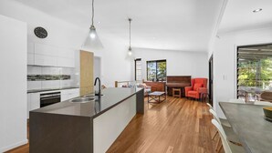 A modern kitchen with a central island, a dining area with a piano, and a red armchair.