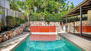 A swimming pool with a stone wall and steps leading up to a covered area.