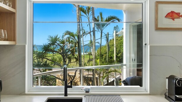 A kitchen with a large window overlooking a tropical garden and ocean view.