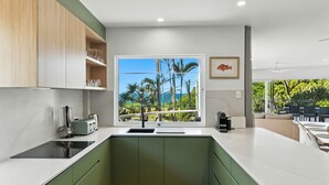 A modern kitchen with a large window overlooking a tropical landscape, equipped with a sink, a toaster, and a coffee maker.