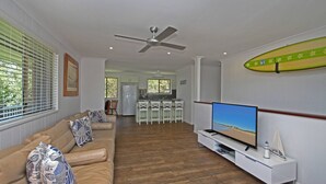 Uma sala de estar com um sofá bege, uma TV de tela plana e um ventilador de teto.