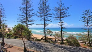 A coastal road with a view of the ocean and beach, lined with trees and a wooden fence. - Unit 4 'The Rocks', Coolum Beach (Coolum Beach)