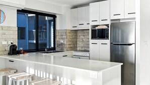 Une cuisine moderne avec des meubles blancs, un réfrigérateur en acier inoxydable, un four à micro-ondes encastré et un grand îlot central doté d’un évier.