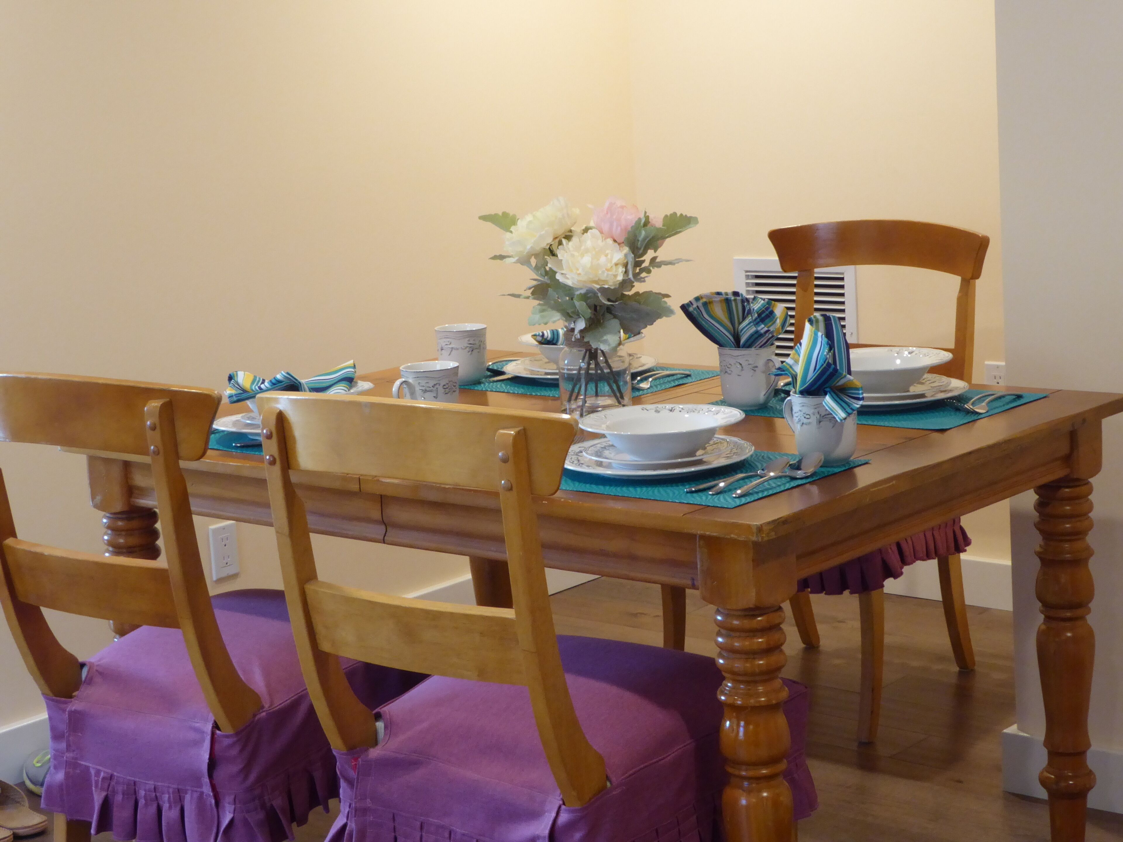 Taula de dinar de fusta amb caires, un vas amb flors i diversos plats i utensilis.