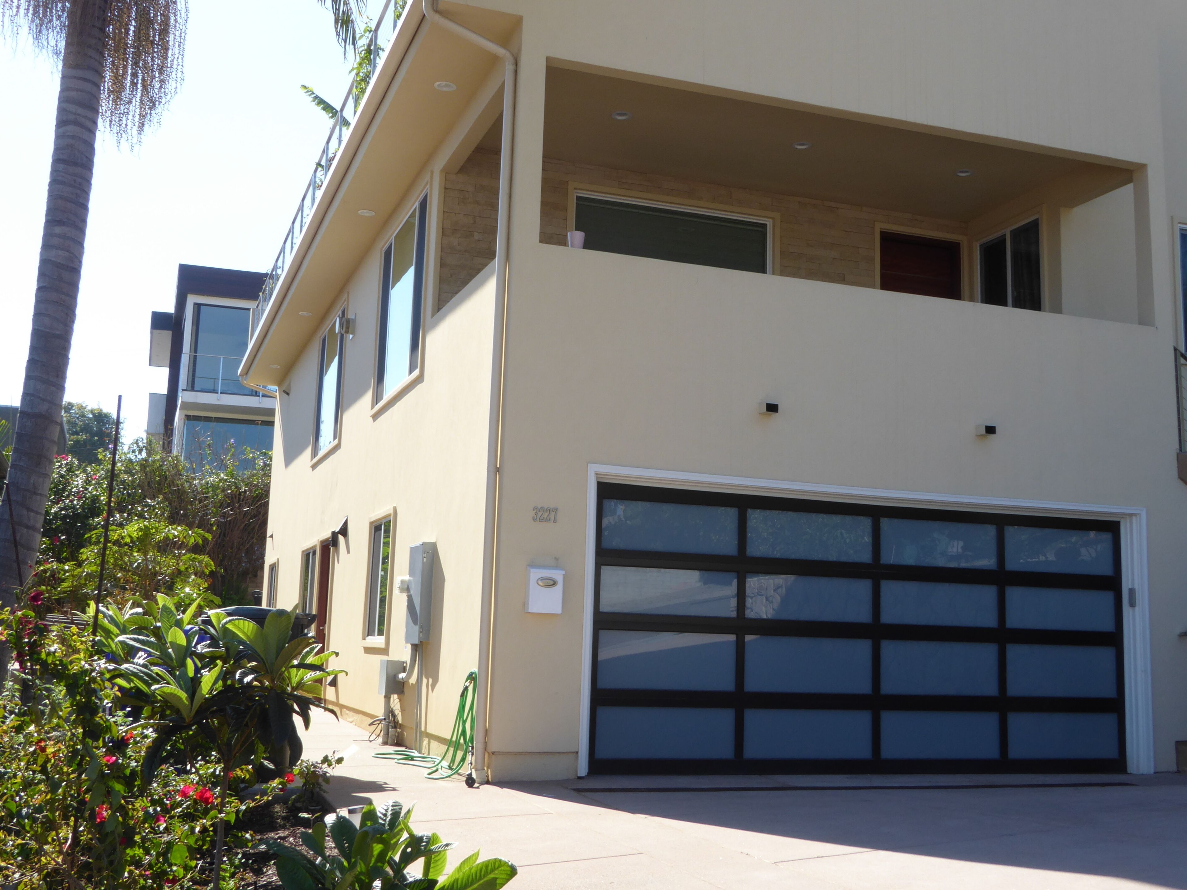 A modern two-story building with a large garage door, a balcony, and a number '3227' on the wall.