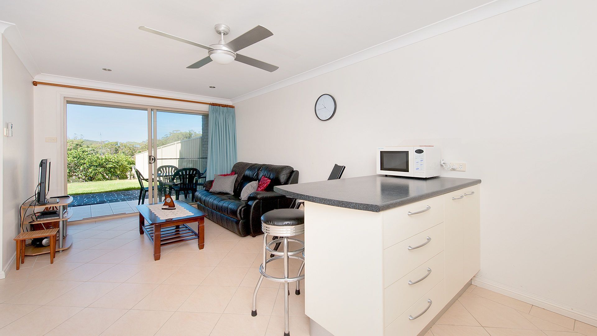 A modern kitchen with a microwave, a dining area with a table and chairs, and a living area with a sofa and a ceiling fan.