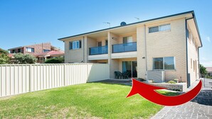 A two-story residential building with a balcony, a fenced backyard, and a paved driveway.