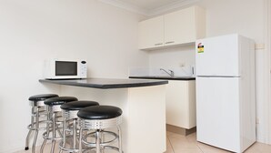 A compact kitchen with a white refrigerator, a microwave, a sink, and four bar stools.