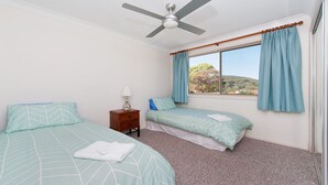 A bedroom with two beds, a ceiling fan, a nightstand, and a window with curtains.