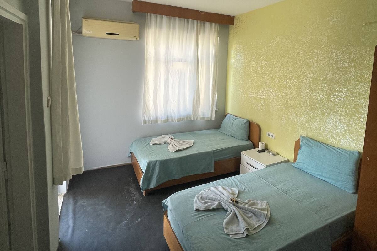 A room with two beds, a window with curtains, a ceiling light, and a wall-mounted air conditioner.