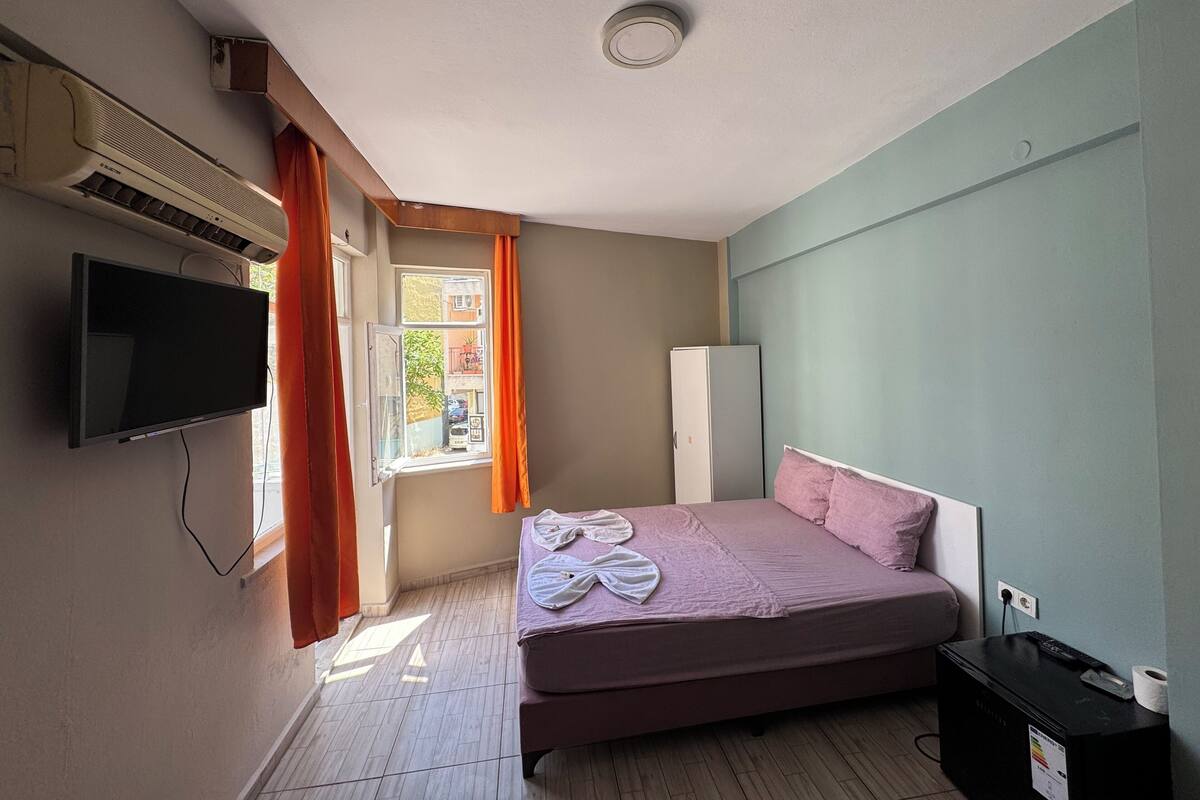 A bedroom with a bed, a TV, a wardrobe, and a window with curtains.