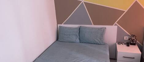 A neatly made bed with two pillows, a bedside table with a plant, and a wall with a geometric pattern.