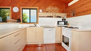 Een compacte keuken met houten wanden, een raam met uitzicht, een spoelbak, een magnetron en een vaatwasser.