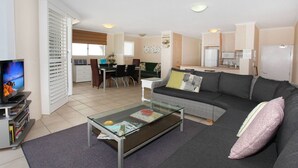 A modern living room with a glass coffee table, grey sofa, and a television on a stand. - Unit 3 'On the Park' at Coolum Beach (Coolum Beach)