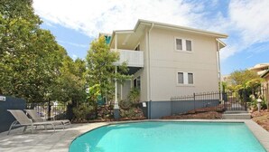 A swimming pool with lounge chairs, a two-story building with a balcony, and a fenced garden area. - Unit 3 'On the Park' at Coolum Beach (Coolum Beach)
