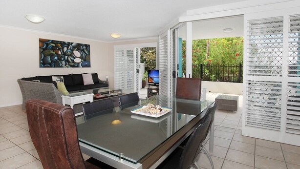 A modern living room with a glass dining table, a sofa, and a TV. - Unit 3 'On the Park' at Coolum Beach (Coolum Beach)