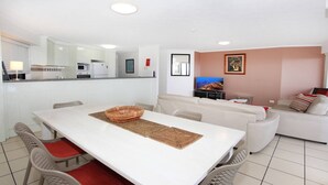 Un saló modern amb un sofà blanc, una taula de dinar amb caires i una cuina al fons.