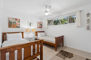Ein Schlafzimmer mit zwei Holzbetten, einem Deckenventilator, einem Fenster mit Vorhängen und Wandbildern.