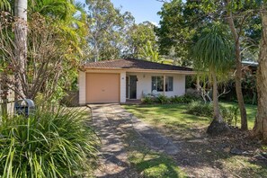 Ein eingeschossiges Haus mit Garage, umgeben von einem Garten mit verschiedenen Pflanzen und Bäumen.