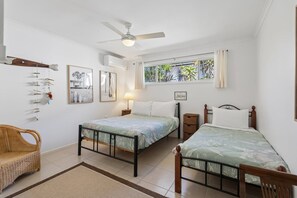 Un dormitorio con dos camas, un ventilador de techo, una ventana con cortinas y obras de arte colgadas en la pared.