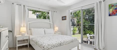 A bedroom with a bed, nightstands, a ceiling fan, and a view of the outdoors.