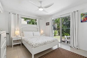 Ein Schlafzimmer mit einem Bett, Nachttischen, einem Deckenventilator und Blick ins Freie.