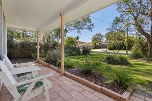 Un espacio al aire libre techado con patio, mobiliario y vistas a un jardín cuidado y una zona residencial.