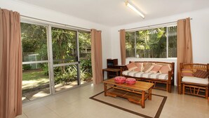 Ein geräumiges Wohnzimmer mit einer Couch, einem Couchtisch und einem Holzstuhl. Große Fenster bieten Blick auf den Garten.